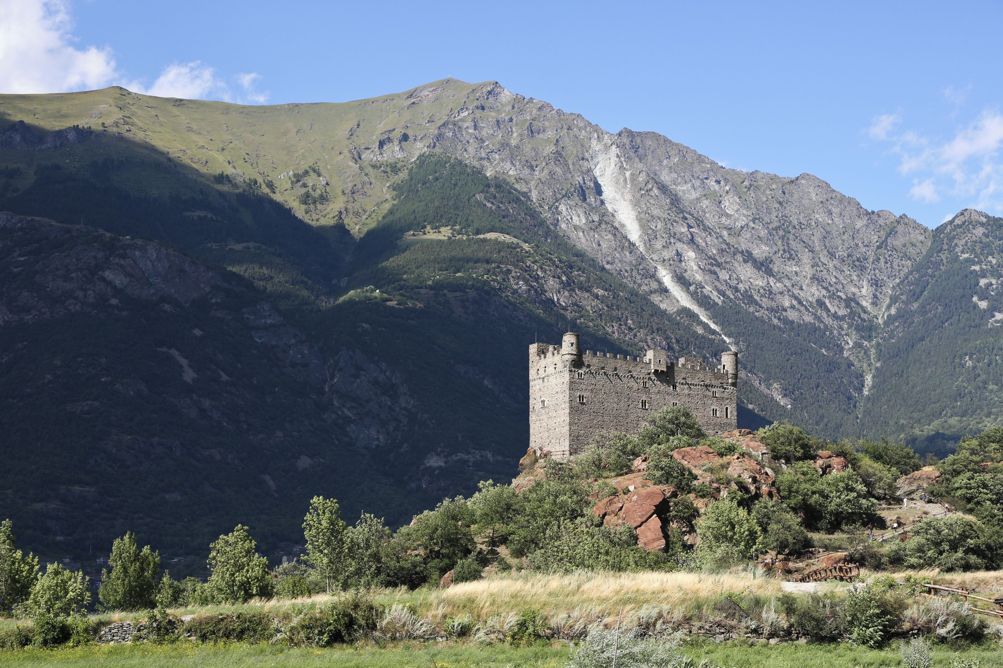 Eine Burg auf einem Hügel vor einer Bergkulisse.
