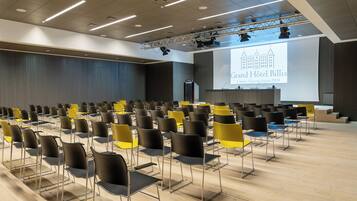 Ein Konferenzraum mit Reihen von Stühlen, einer Bühne mit einer Präsentationsleinwand und einem Rednerpult.