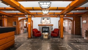 A log cabin interior with a stone fireplace, wooden beams, and a stone floor. - Le Lodge de la Montagne - Les Suites Tremblant (Mont-Tremblant)