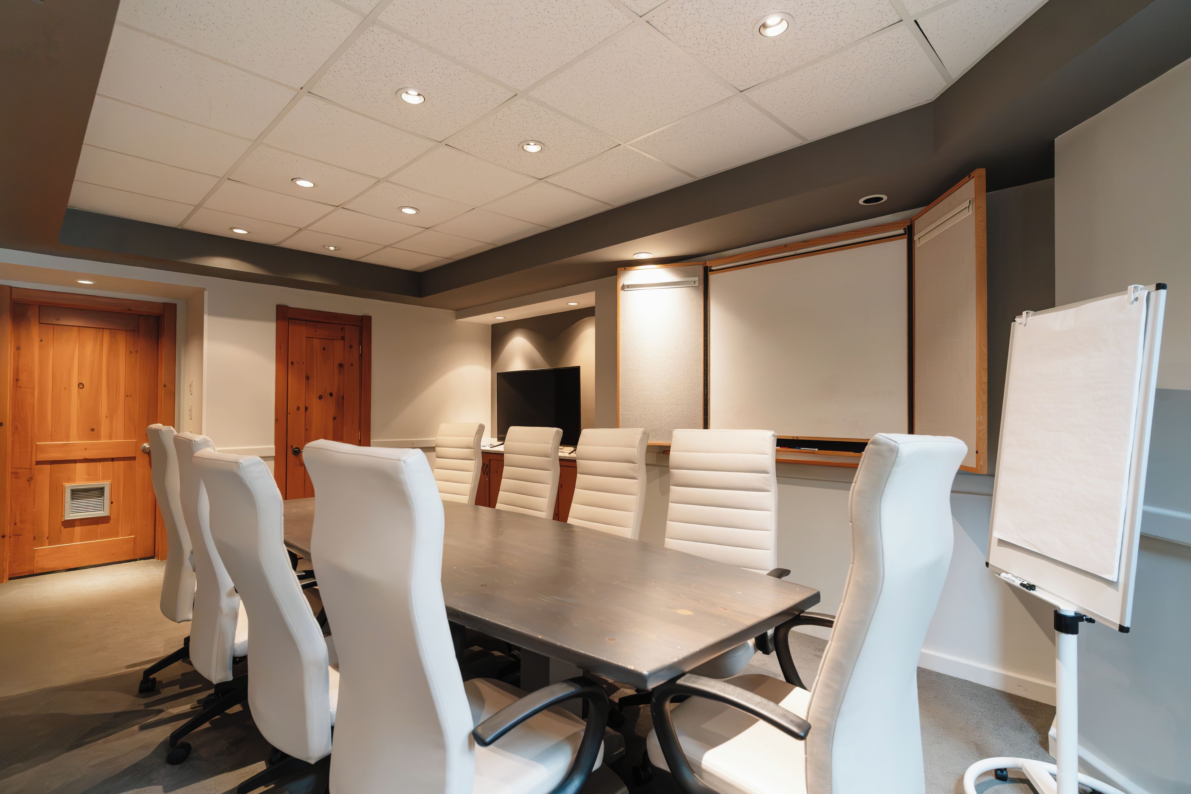 A conference room with a long table, white chairs, a whiteboard, and a television.