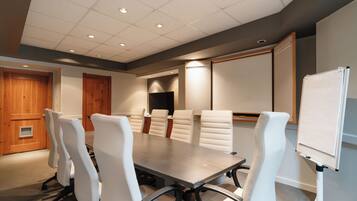 A conference room with a long table, white chairs, a whiteboard, and a television.
