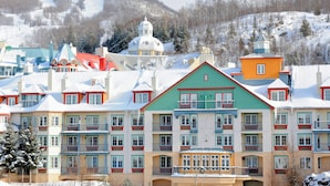 A multi-story hotel with colorful facades, balconies, and a snowy mountain backdrop. - Le Lodge de la Montagne - Les Suites Tremblant (Mont-Tremblant)