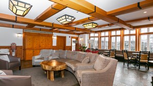 A spacious lobby with a large sectional sofa, a wooden coffee table, and a stone floor. There are multiple tables and chairs arranged for dining or meetings. - Le Lodge de la Montagne - Les Suites Tremblant (Mont-Tremblant)