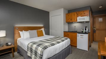 A hotel room with a bed, bedside table, and a kitchenette area including a microwave and coffee maker.
