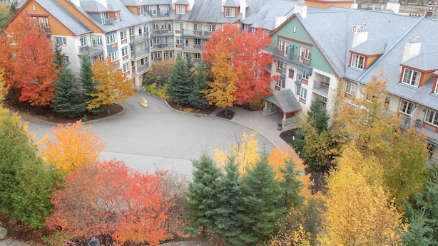 A multi-story hotel with a central courtyard surrounded by colorful autumn trees. - Le Lodge de la Montagne - Les Suites Tremblant (Mont-Tremblant)