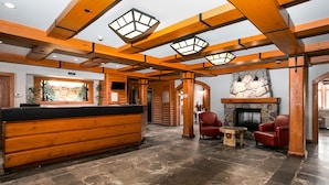 A log cabin-style interior with a reception desk, stone flooring, wooden beams, and a stone fireplace. - Le Lodge de la Montagne - Les Suites Tremblant (Mont-Tremblant)