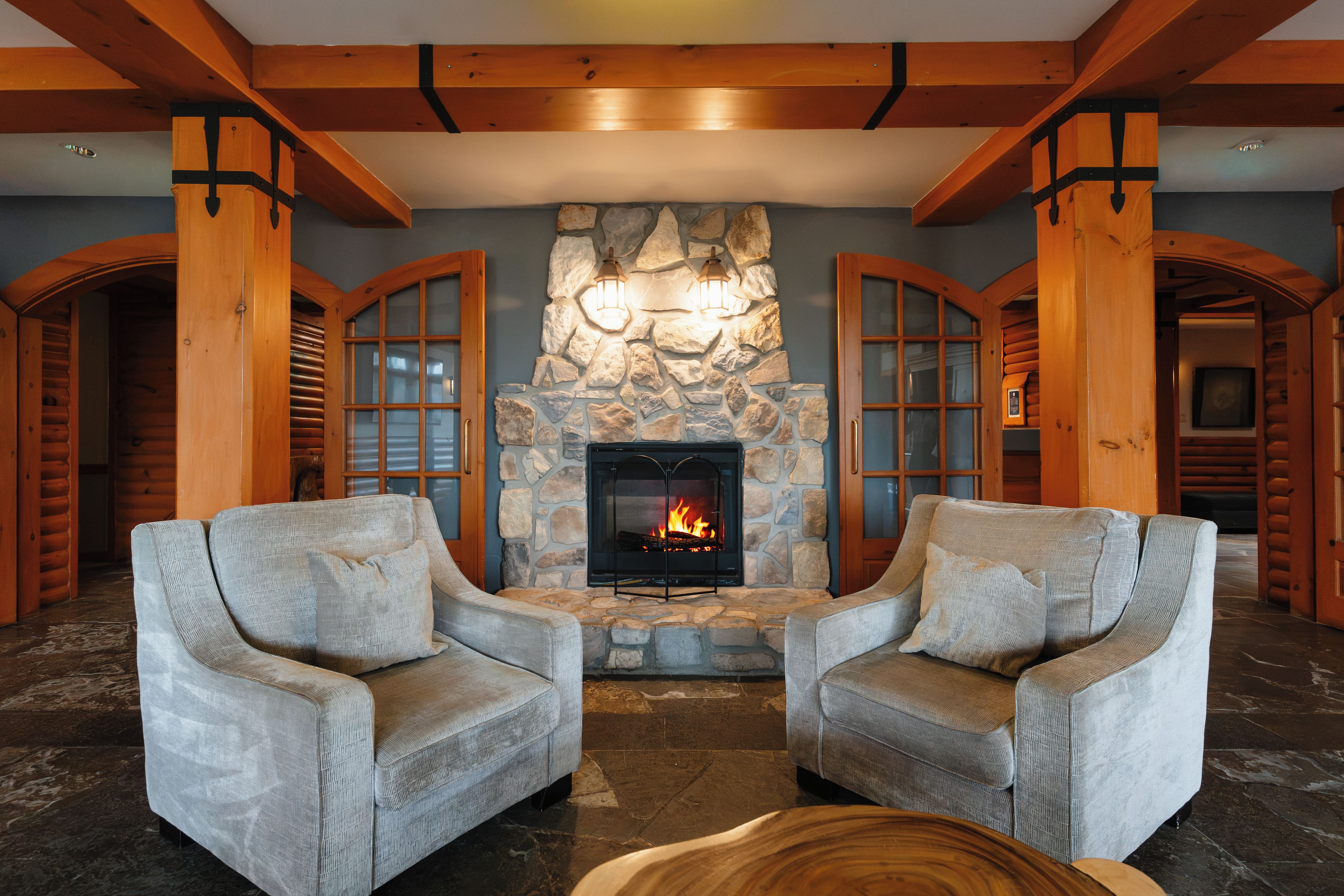 Un intérieur chaleureux avec une cheminée en pierre, deux fauteuils et des poutres en bois.