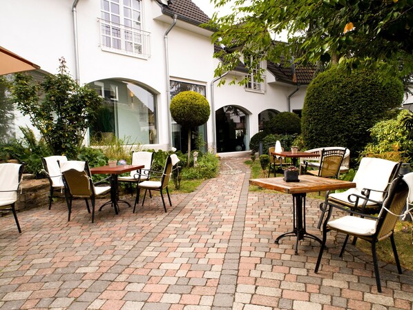 A courtyard with brick flooring, outdoor seating, and greenery. - Romantik Hotel Neuhaus (Iserlohn)
