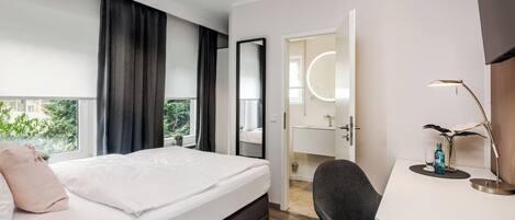 Une chambre d’hôtel moderne, dotée d’un grand lit, d’un bureau, d’une chaise, d’un miroir et offrant une vue sur la verdure environnante.