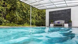 Una piscina con techo de cristal, rodeada de exuberante vegetación y un muro de piedra.