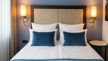 Ein Hotelzimmer mit einem großen Bett, zwei Wandlampen, einem runden Beistelltisch und einem Kopfteil mit Struktur.