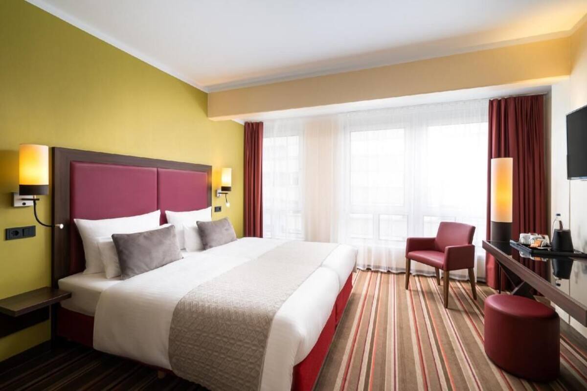 A hotel room with a large bed, a desk, a chair, and a TV.
