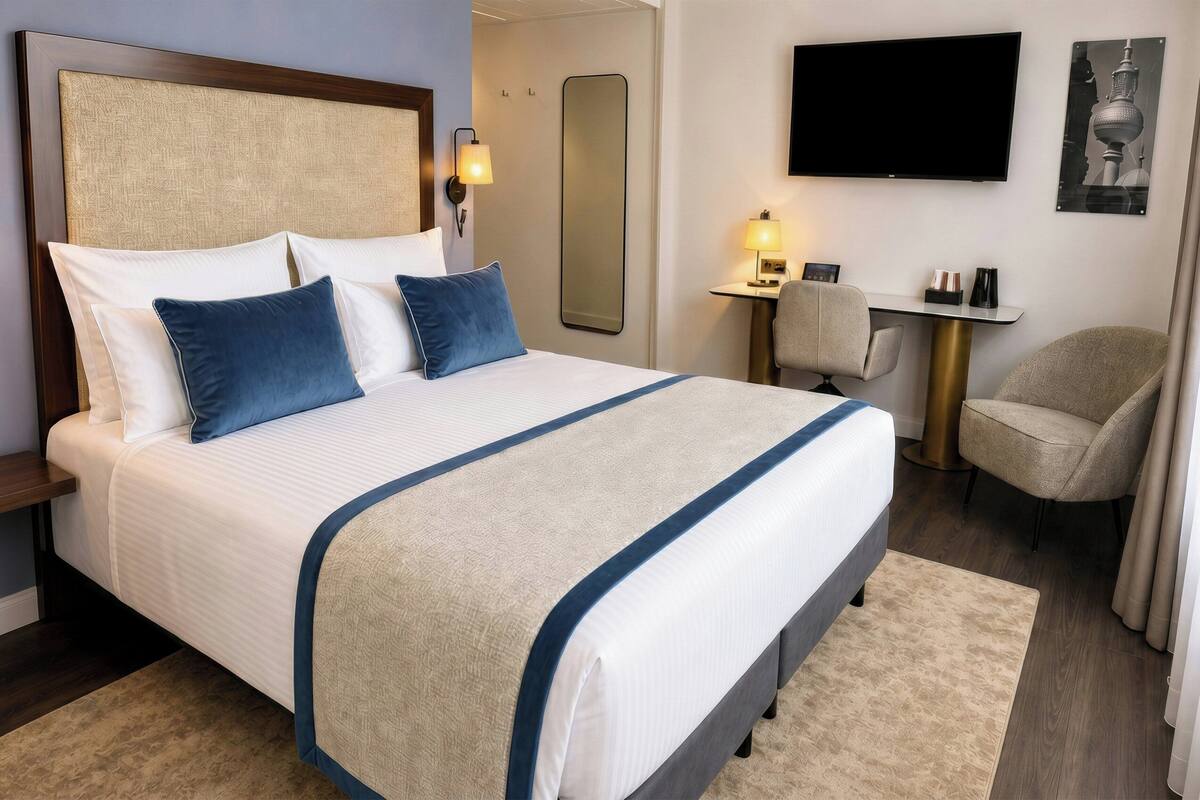A hotel room with a large bed, a desk, a chair, a TV, and a mirror.