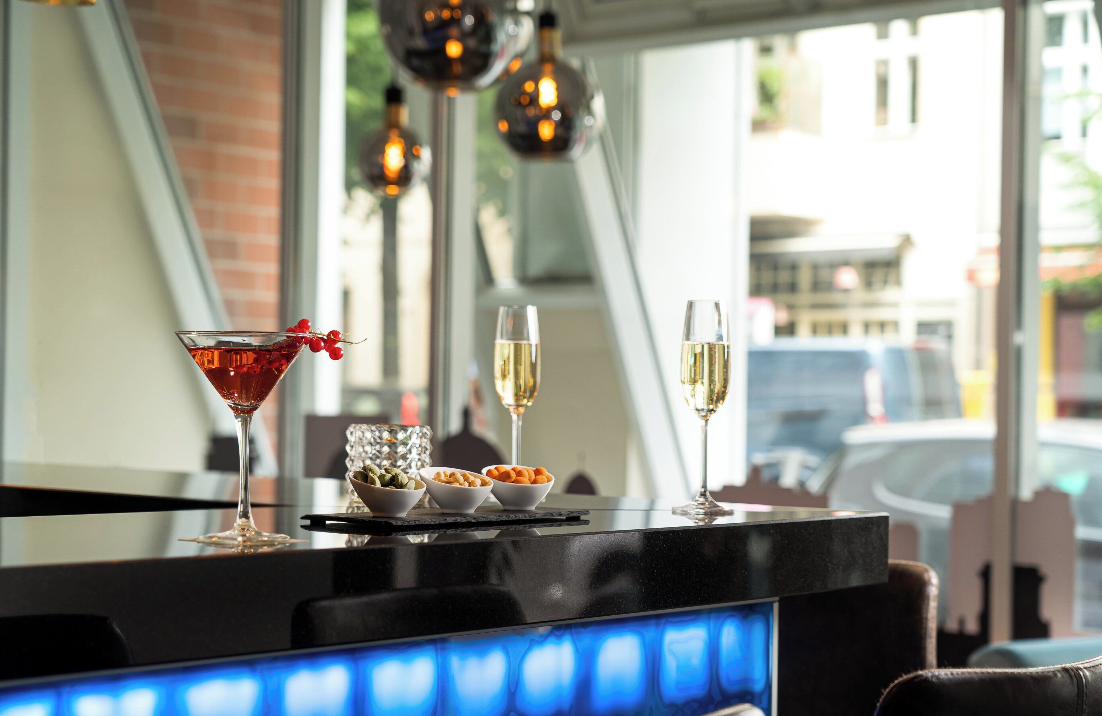 Eine Bar mit einem roten Cocktailglas, zwei Weingenüssen und Schalen mit Nüssen und Trockenfrüchten.