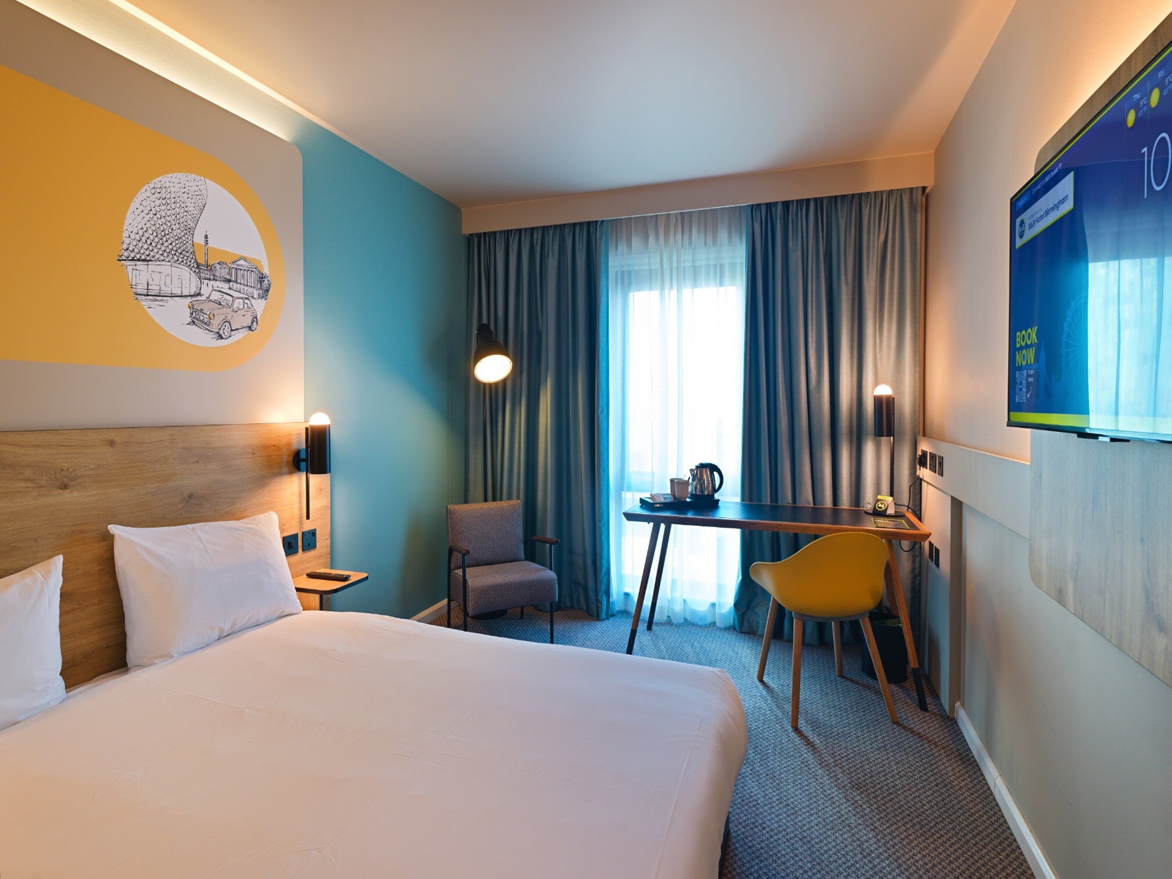 Een hotelkamer met een groot bed, een bureau, een stoel, een televisie en een raam met gordijnen.