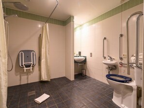 Une salle de bain équipée d’une douche, de toilettes avec un siège surélevé, d’un lavabo et d’une barre d’appui.