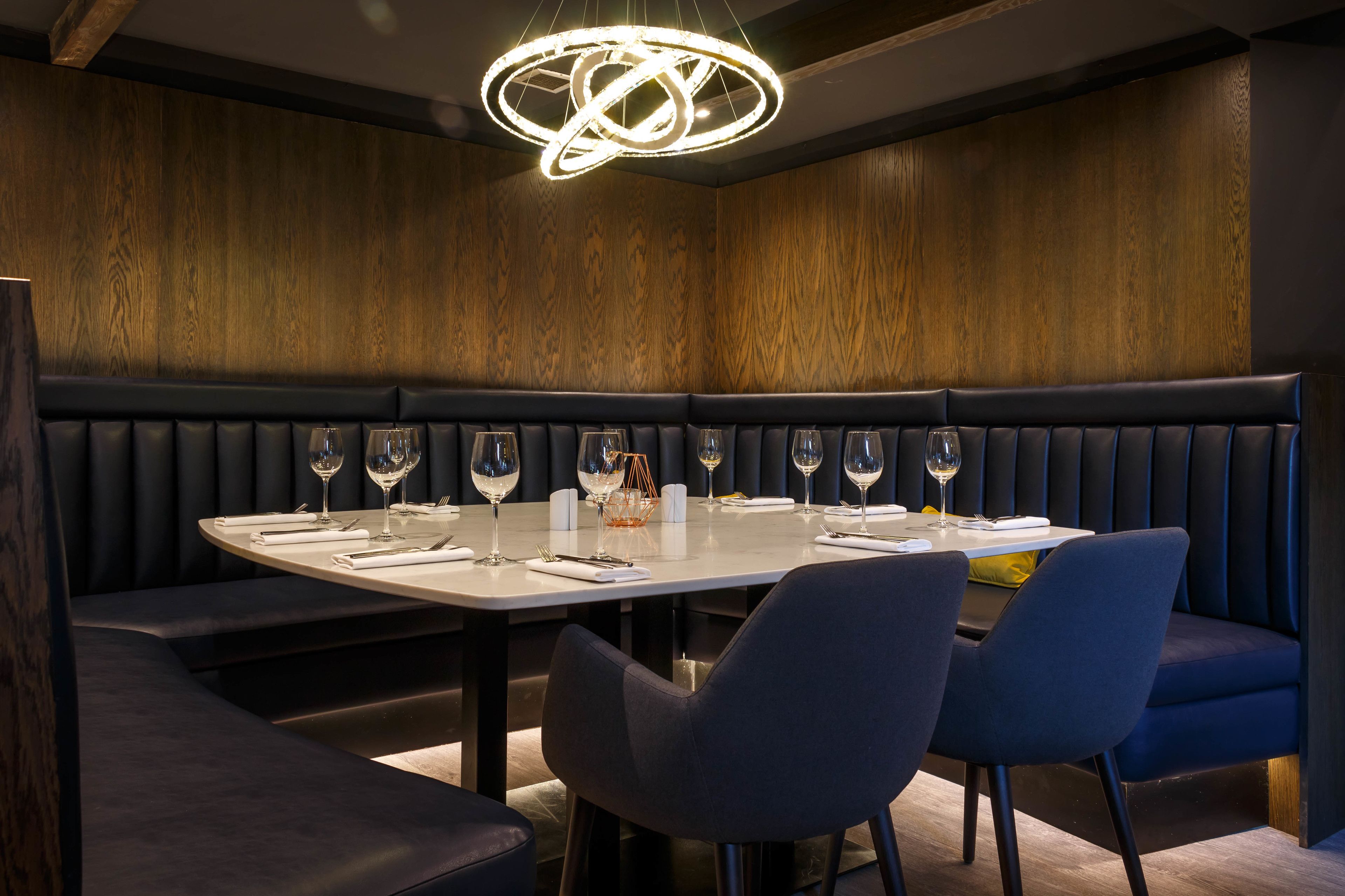 Un ristorante con un lungo tavolo apparecchiato per la cena, comode panche imbottite e un lampadario moderno.