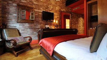 A room with a brick wall, a wooden bed, a bench, a television, and a mirror.