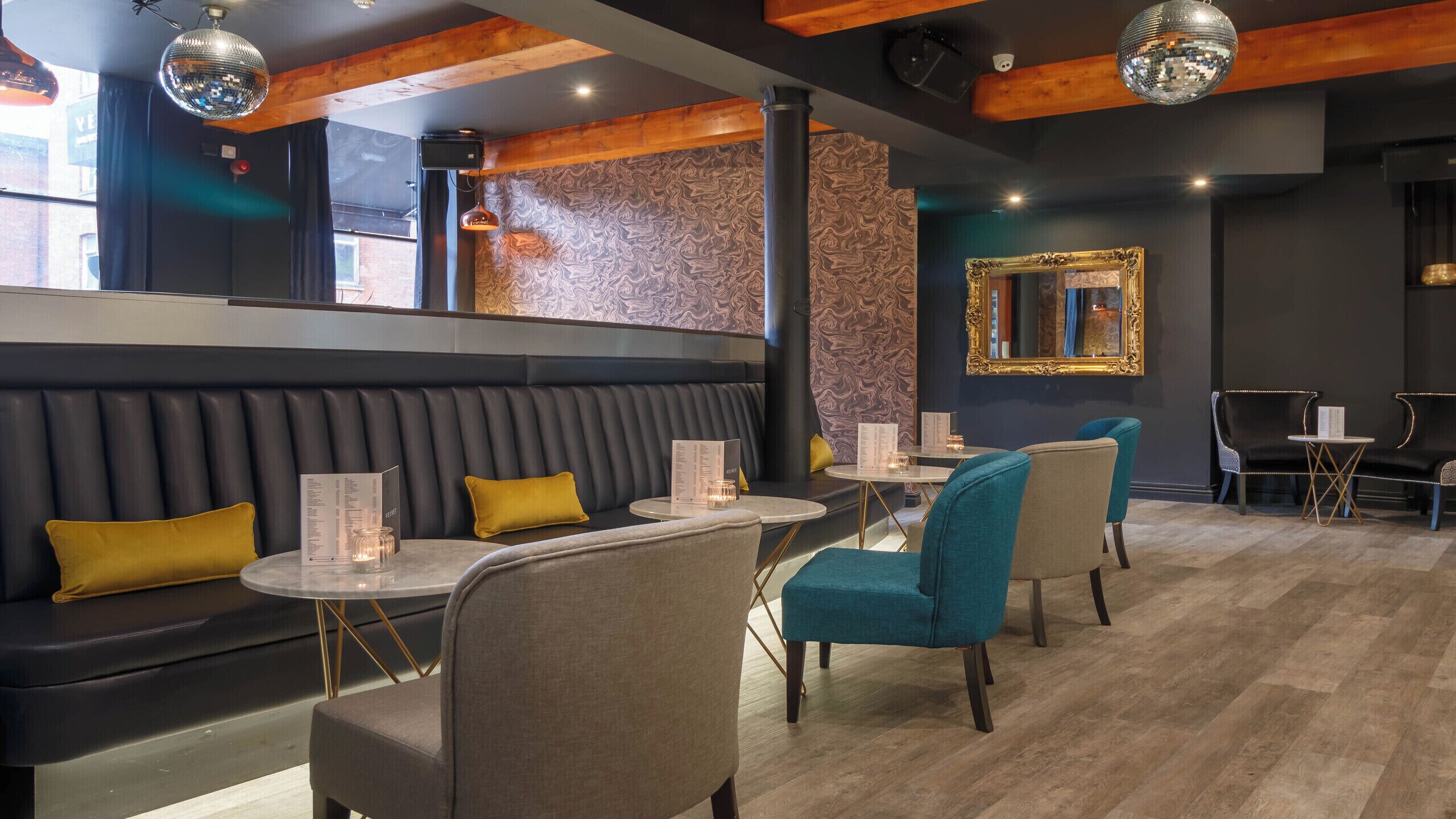 A restaurant with a dark-colored booth seating area, round tables with chairs, and a mirror on the wall.