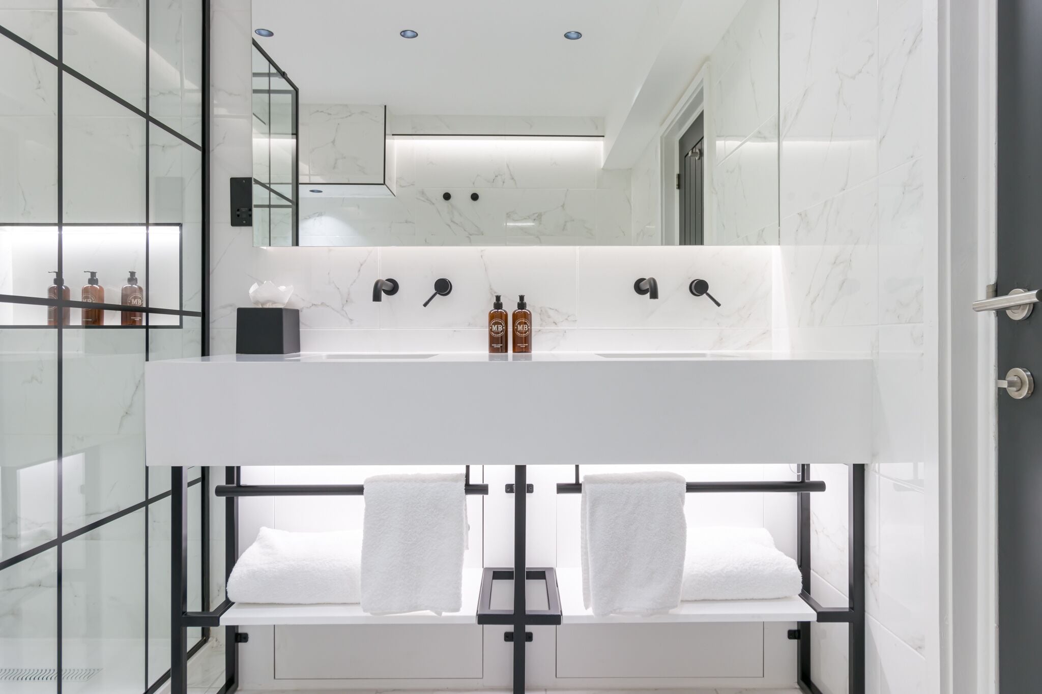 A modern bathroom with a white vanity, two sinks, a large mirror, and a glass shower enclosure.
