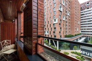 Un balcone con soffitto in legno, una sedia in metallo e vista su un edificio moderno con diverse finestre e un cartello con la scritta "MPSU".