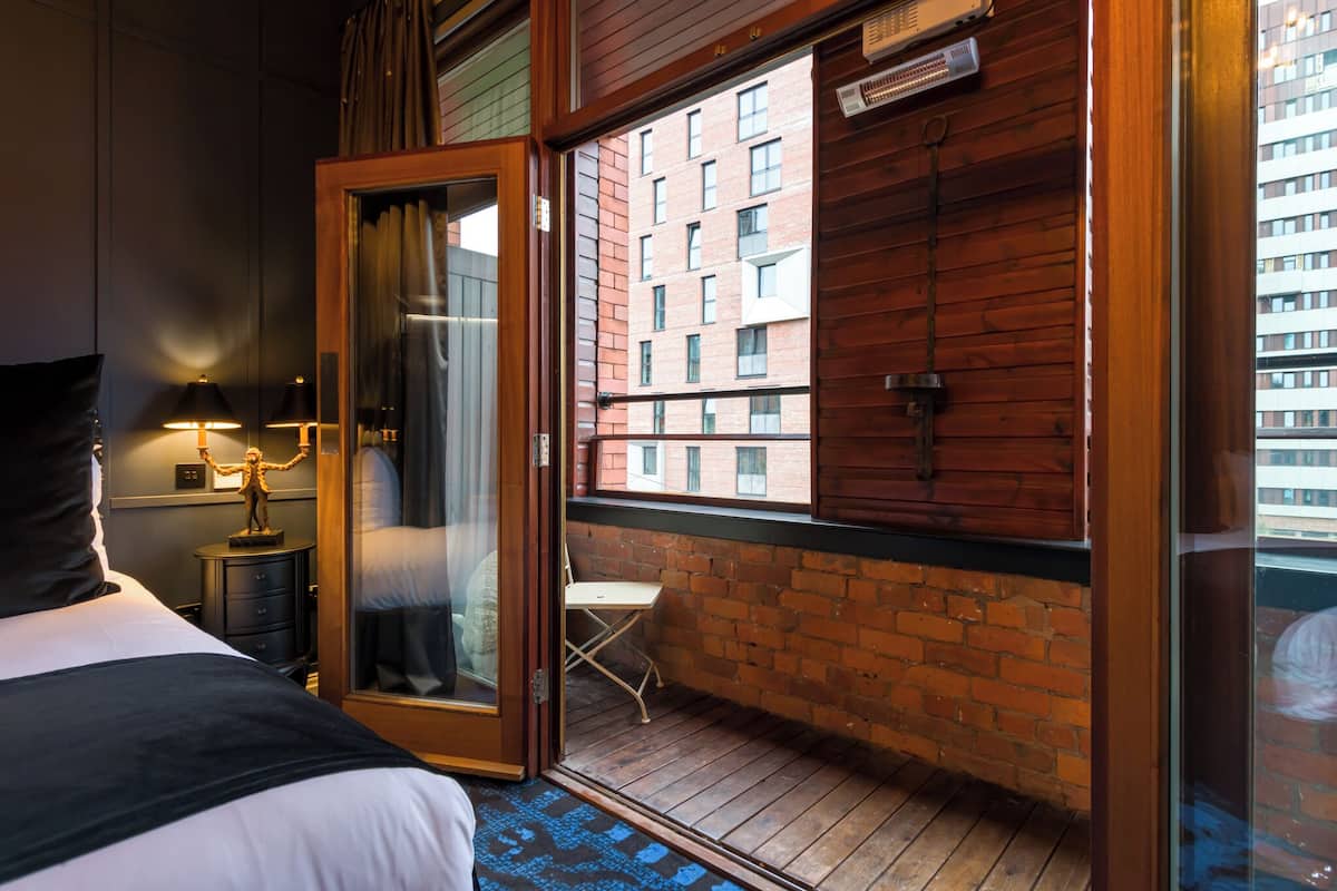 A hotel room with a large window, a bed, a nightstand, a lamp, and a small table with a statue.