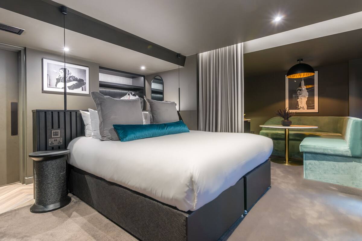A modern bedroom with a large bed, a small side table, a chair, and a wall-mounted TV.
