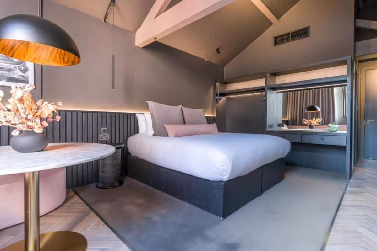 A modern bedroom with a large bed, bedside table, and a mirror.