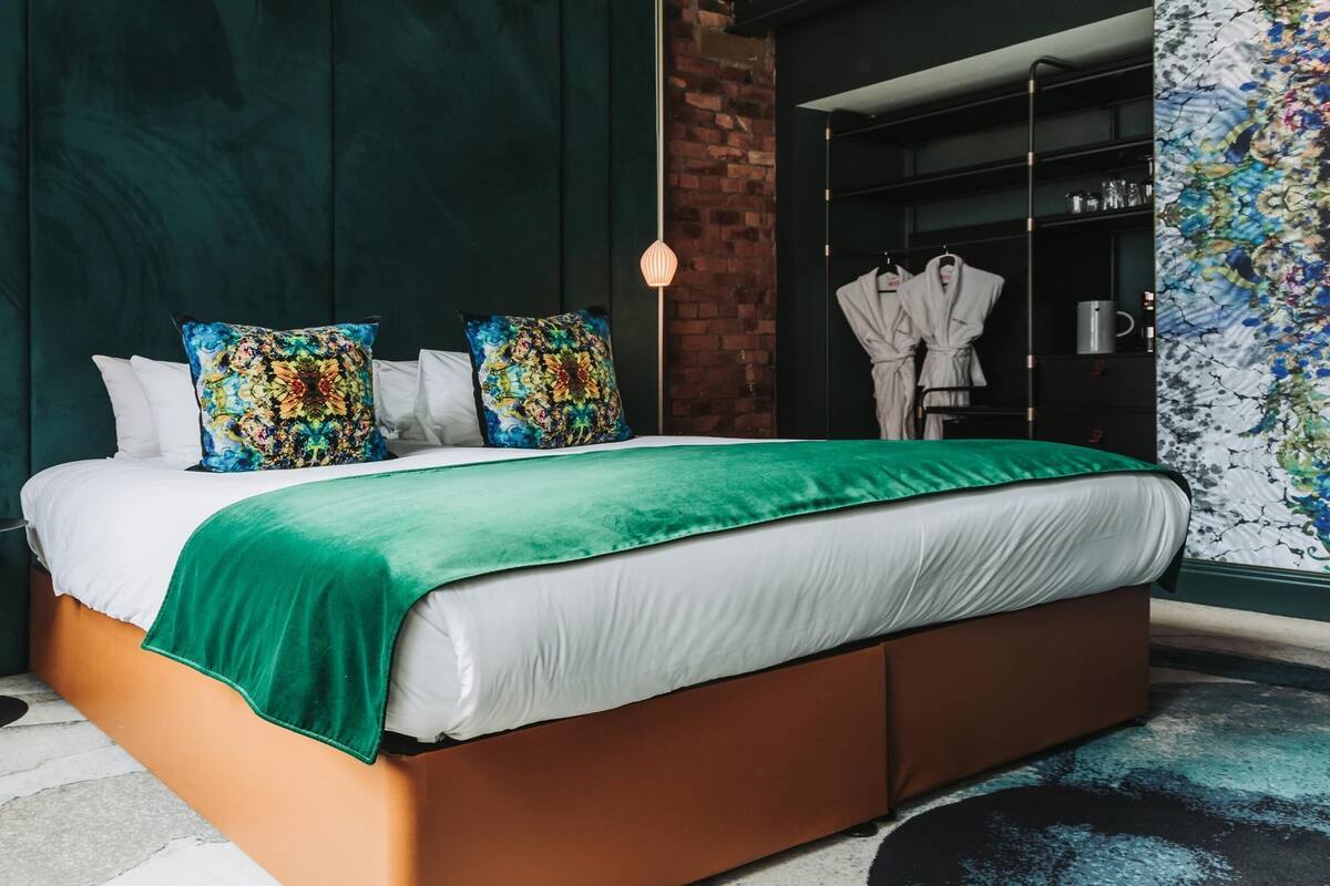 A modern bedroom with a large bed, green bedding, and colorful pillows.