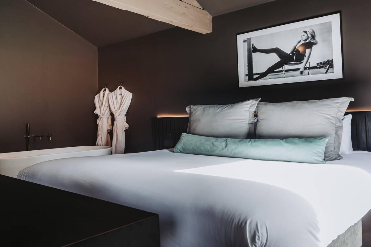 A modern bedroom with a large bed, a bathtub, and a framed picture on the wall.