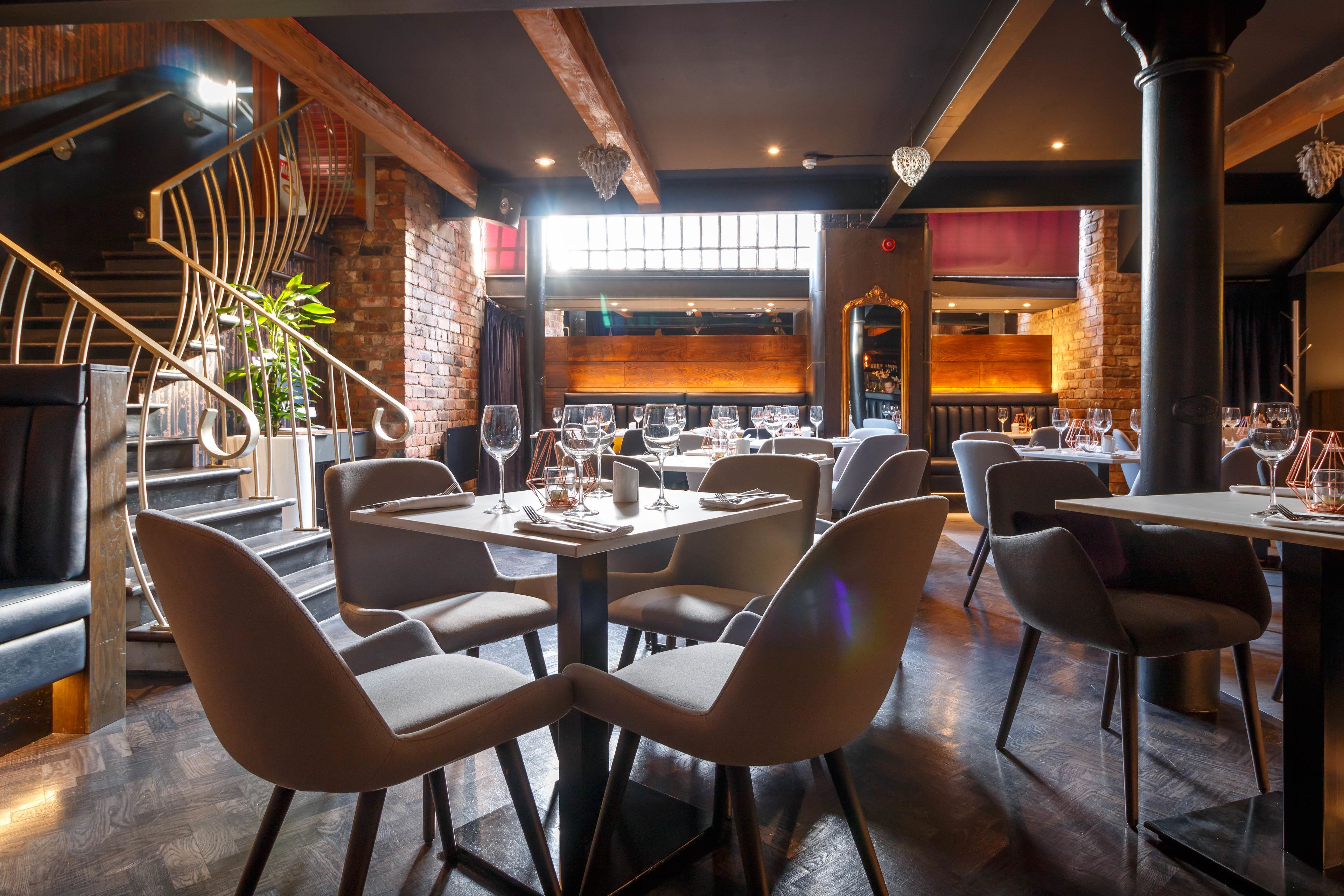 A restaurant with modern decor, featuring a mix of brick and wood elements, and a staircase leading to an upper level.