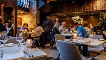 A restaurant with tables set for dining, a brick wall, and a large mirror.