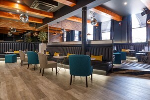 Un interior moderno con vigas de madera, asientos acolchados negros, sillas color turquesa e iluminación colgante.