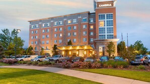 Un hôtel à plusieurs étages, reconnaissable à son grand panneau « CAMBRIA », un parking avec plusieurs voitures et une pelouse bien entretenue.