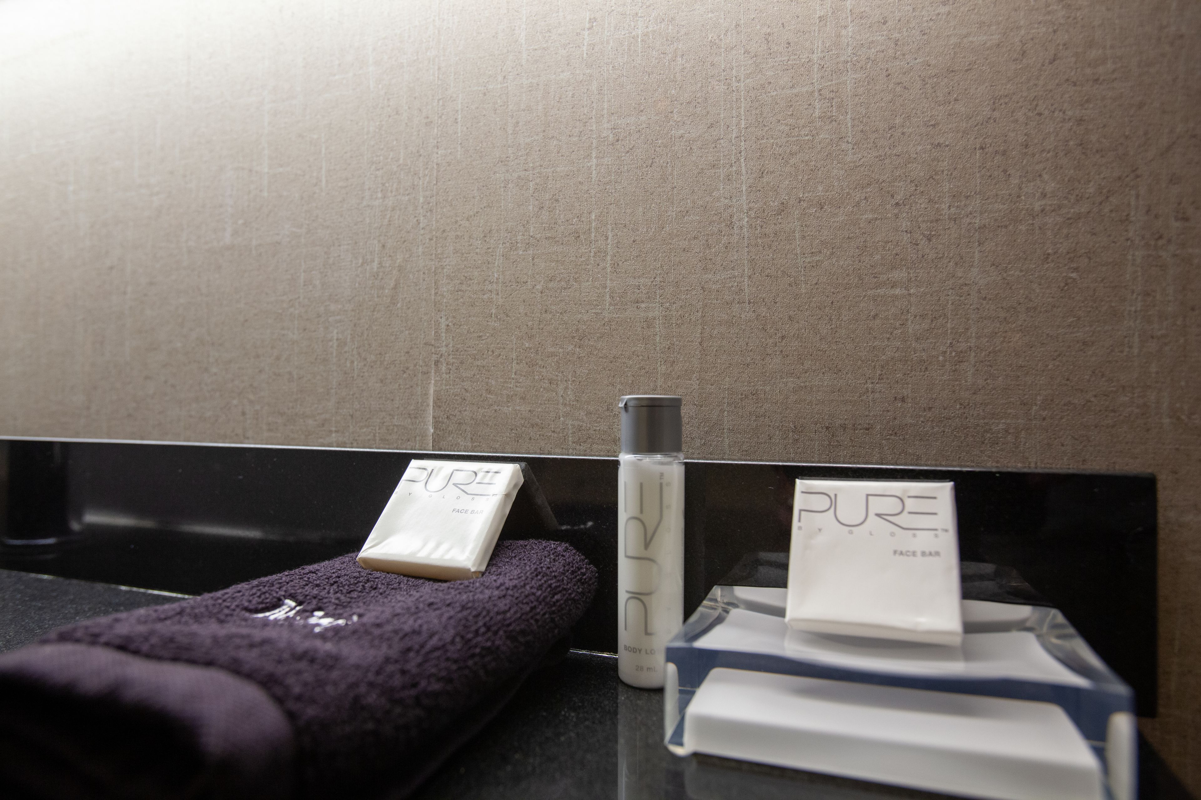 A bathroom with a black sink, a purple towel, and a bottle of Pure body lotion.