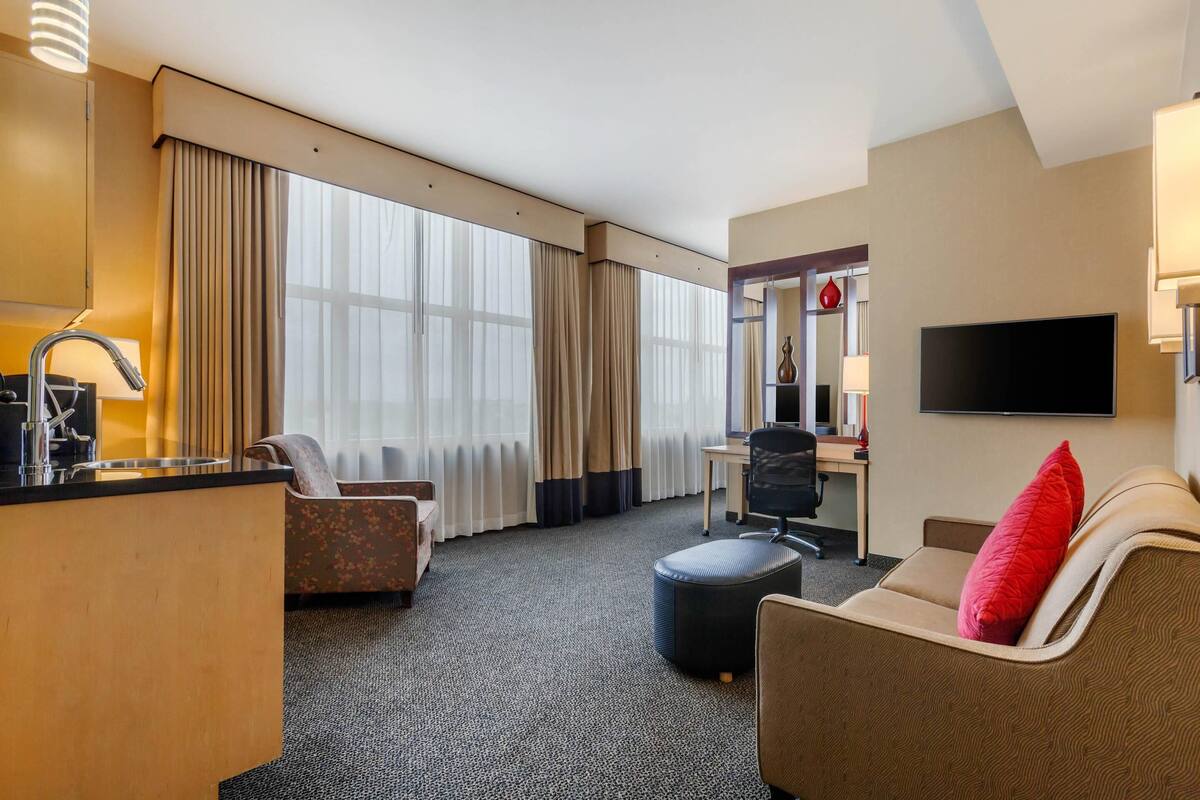 Habitación de hotel con kitchenette, sofá, sillón, escritorio y televisión.