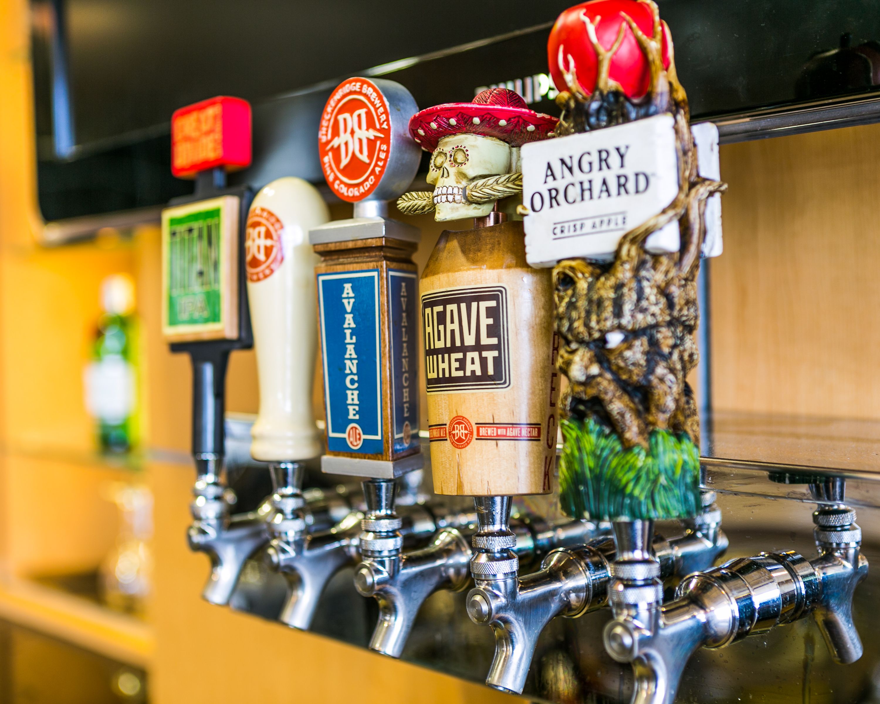 A bar with multiple taps, each labeled with different beer names like 'Avalanche,' 'Agave Wheat,' and 'Angry Orchard.'