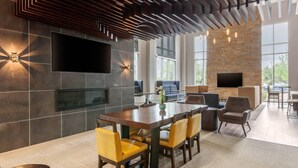 Un intérieur moderne avec une grande table à manger, des chaises jaunes, un téléviseur à écran plat fixé au mur et un mur d’accent en pierre.