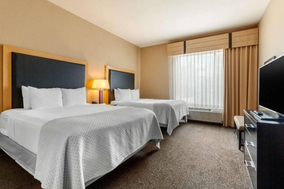 Habitación de hotel con dos camas, televisión, escritorio y ventana con cortinas.