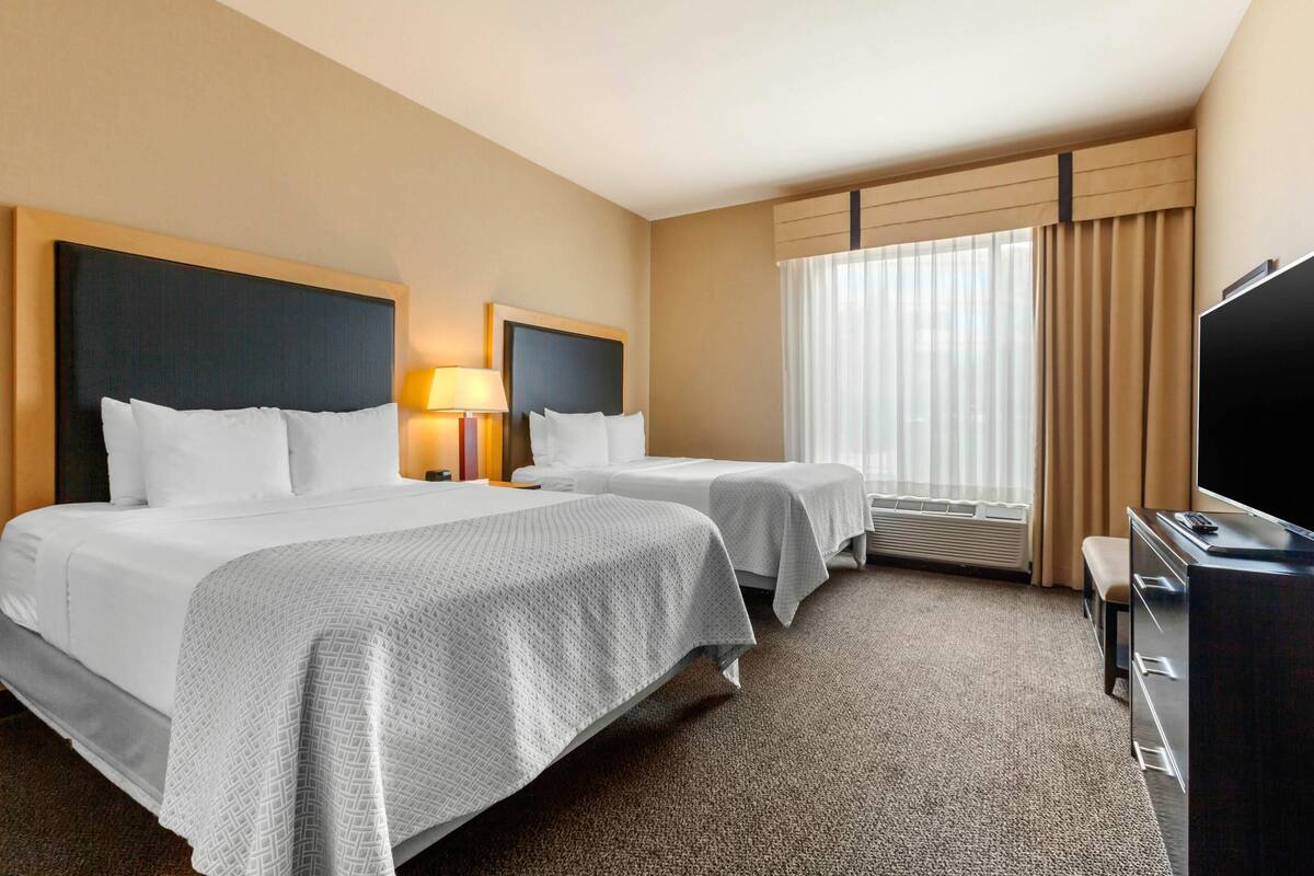 Habitación de hotel con dos camas, televisión, escritorio y ventana con cortinas.