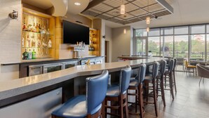Un espace bar moderne doté d’un long comptoir, de tabourets de bar et d’un téléviseur fixé au mur.