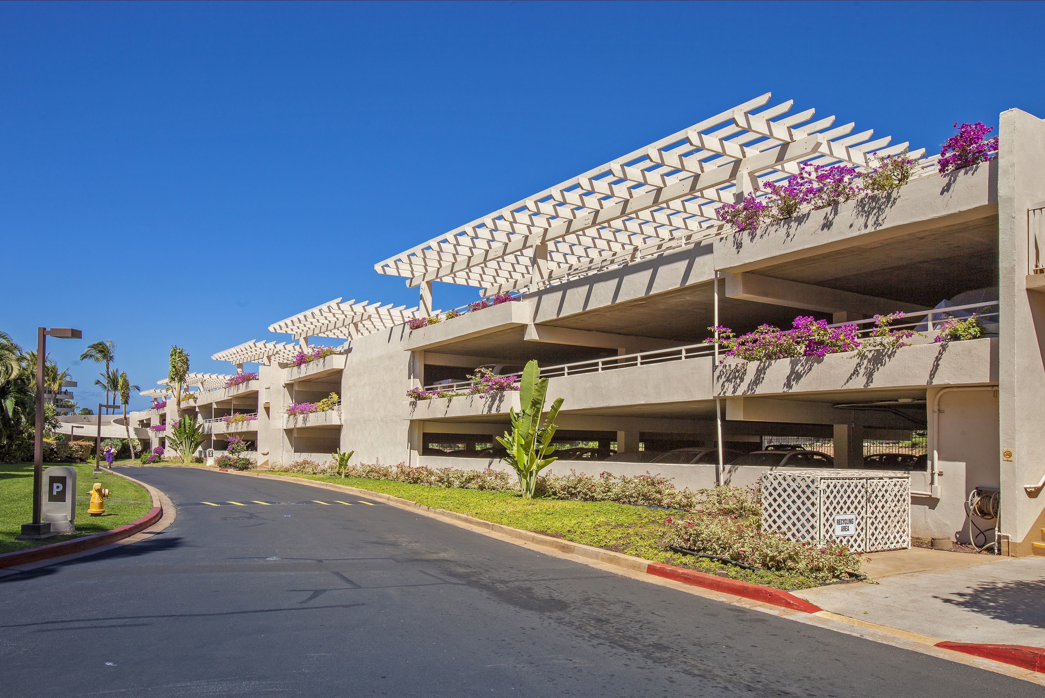 A modern building with a unique geometric facade, outdoor flower arrangements, and a clear blue sky.