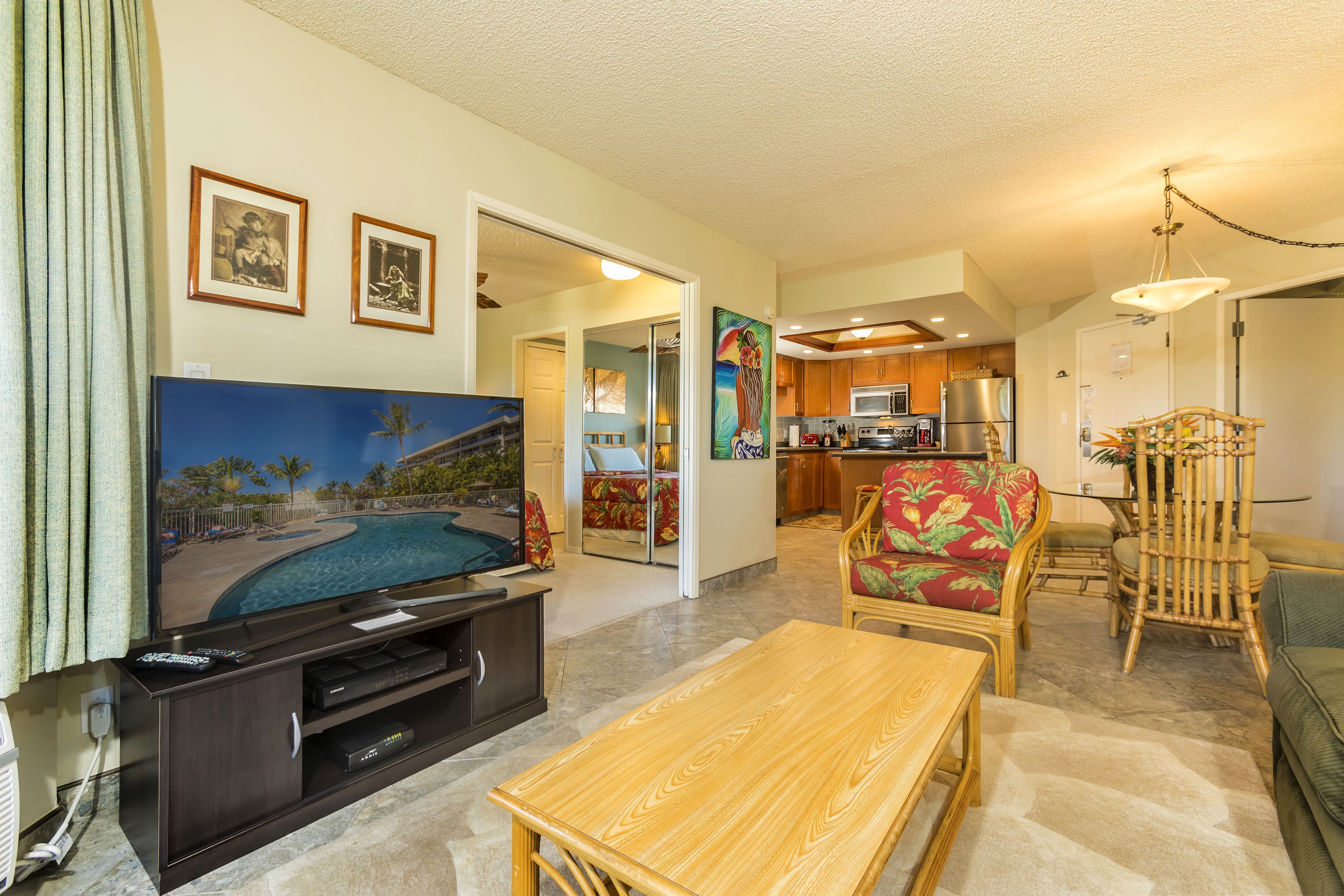 A living room with a flat-screen TV, a wooden coffee table, and a dining area with a bamboo chair.