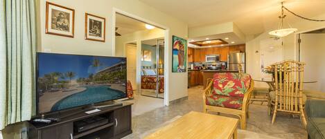 A living room with a flat-screen TV, a wooden coffee table, and a dining area with a bamboo chair.