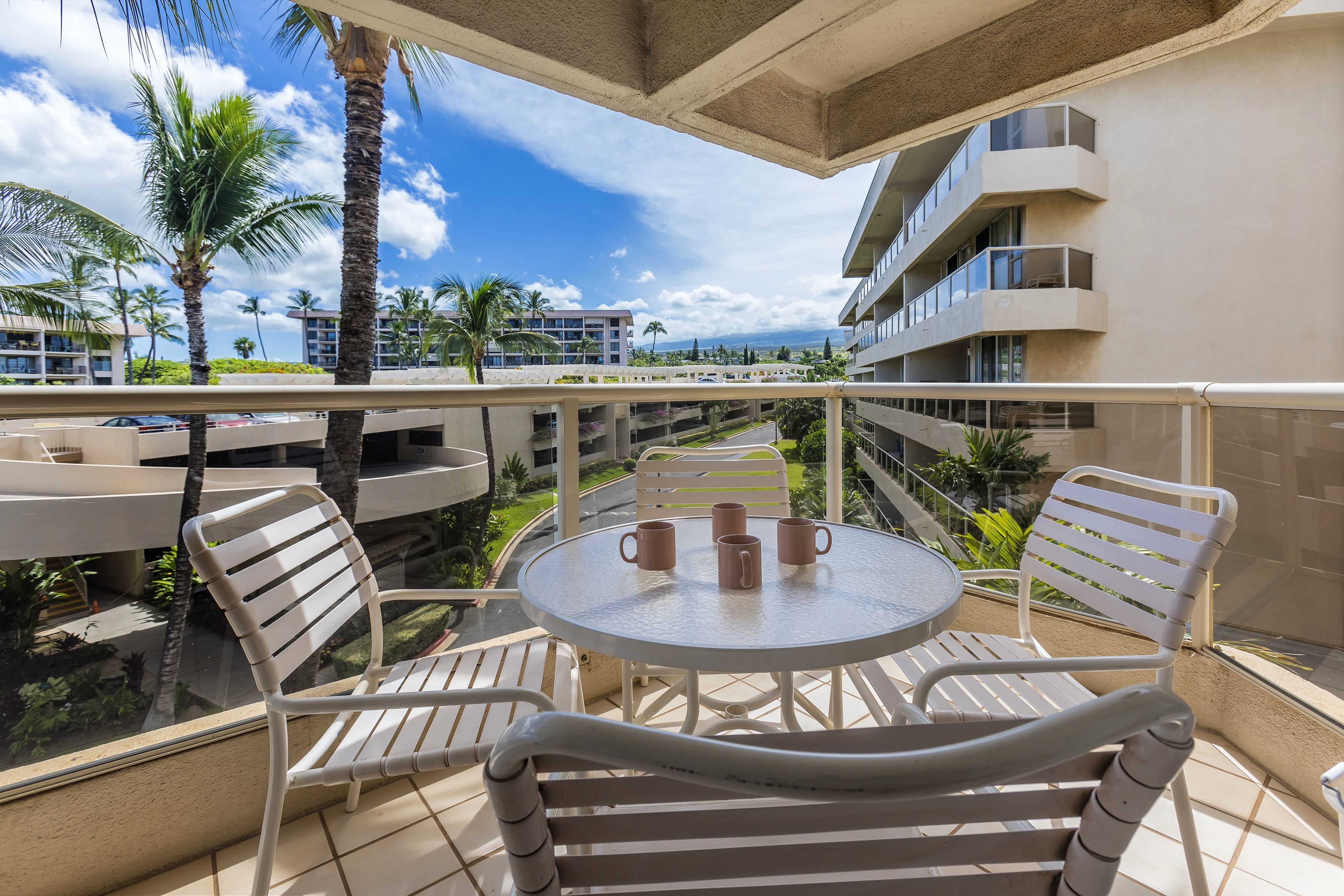 A balcony with a round table and chairs, overlooking a pool and palm trees.