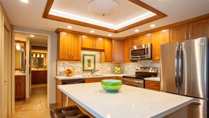 Una cocina moderna con armarios de madera, un refrigerador de acero inoxidable, un microondas y una isla grande con un tazón verde.