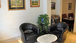 Una habitación con dos sillones de cuero, una mesita redonda y una planta en maceta. Hay cuadros enmarcados en la pared.