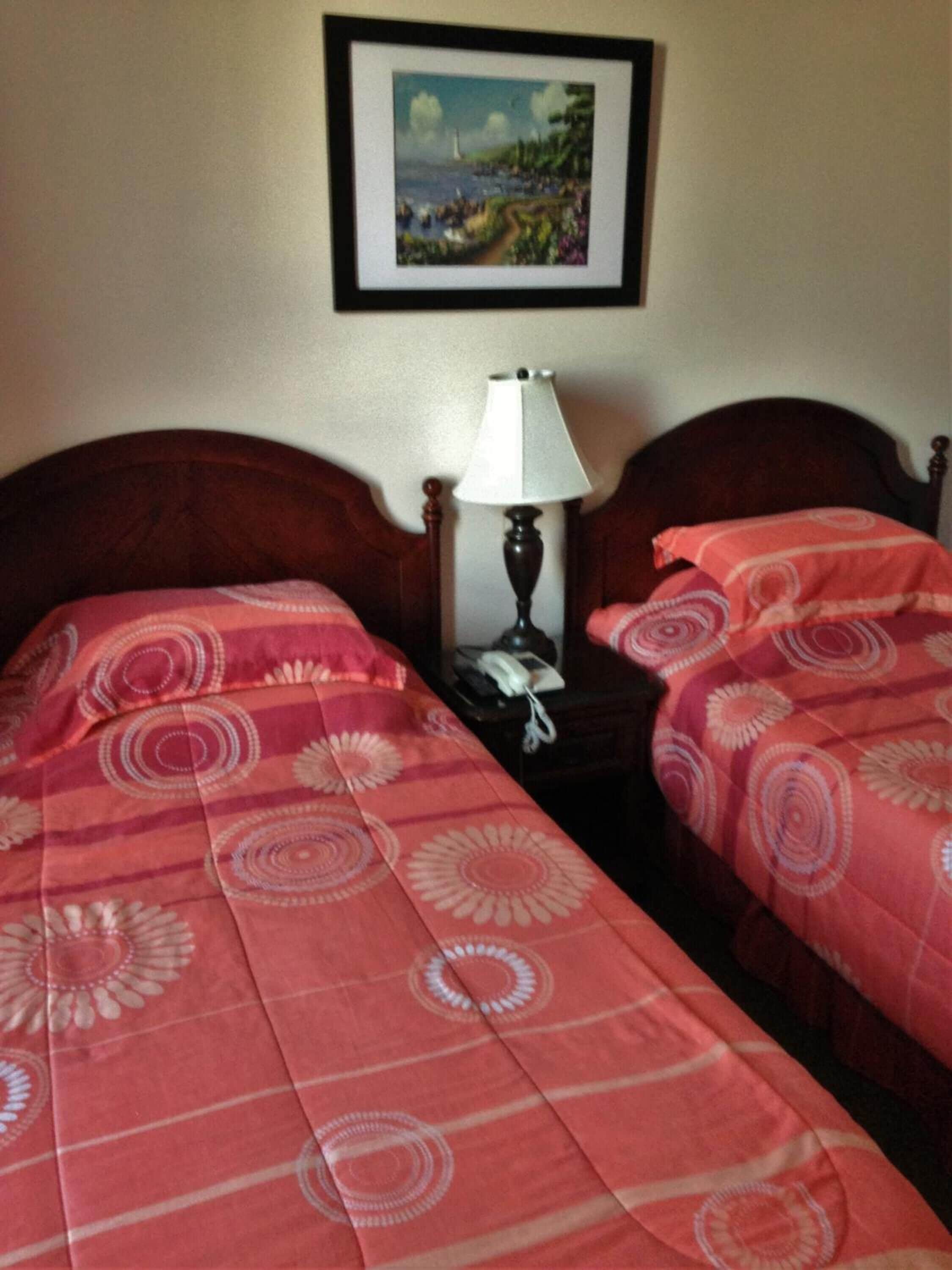 A hotel room with two single beds, each with a red floral bedspread, a wooden headboard, and a nightstand with a lamp and phone.