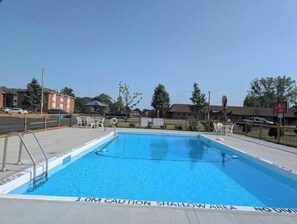 A rectangular swimming pool with a shallow area warning, surrounded by a fenced area with lounge chairs and umbrellas.