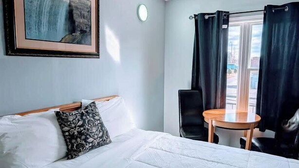 Habitación de hotel con cama, una mesa redonda, una silla, un cuadro en la pared y una ventana con cortinas.